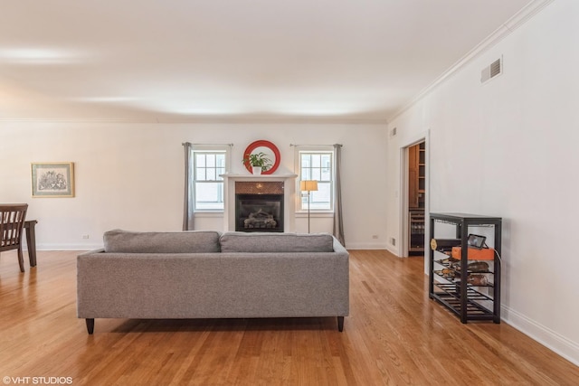 living room featuring baseboards, visible vents, a fireplace, and light wood finished floors