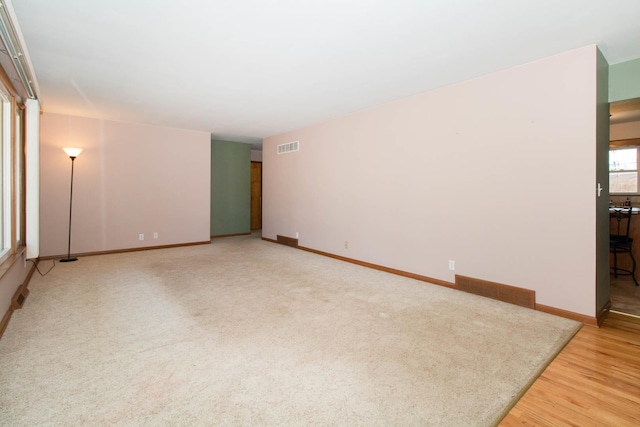 unfurnished room featuring light wood-type flooring, baseboards, visible vents, and light colored carpet