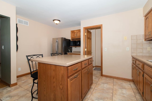 kitchen featuring black microwave, a kitchen island, visible vents, a kitchen breakfast bar, and freestanding refrigerator