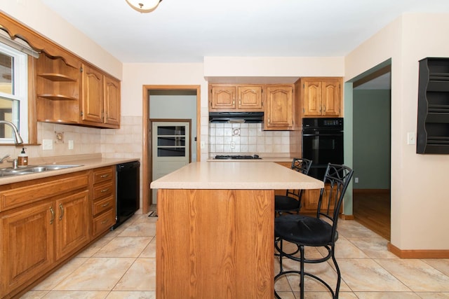 kitchen featuring a breakfast bar area, under cabinet range hood, a kitchen island, a sink, and black dishwasher