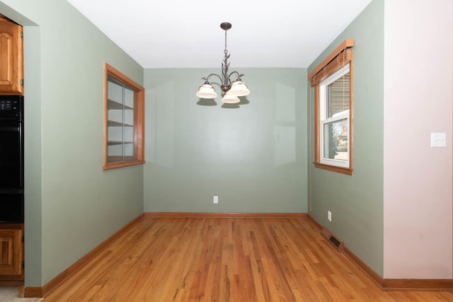 unfurnished dining area featuring baseboards, a notable chandelier, and light wood finished floors