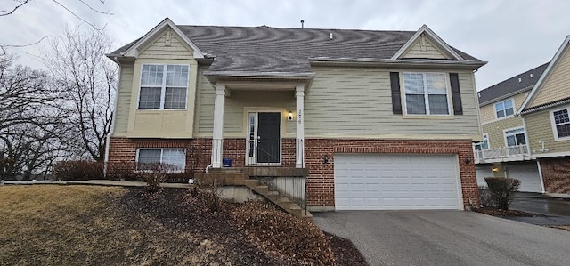 split foyer home featuring aphalt driveway, brick siding, a shingled roof, and an attached garage