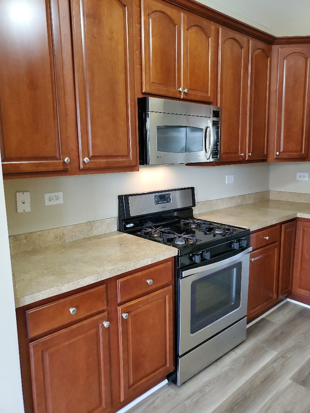 kitchen with stainless steel appliances, brown cabinetry, light countertops, and light wood-style floors