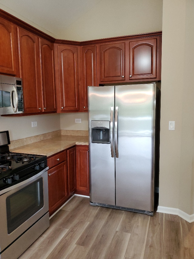 kitchen featuring stainless steel appliances, lofted ceiling, light countertops, light wood-style floors, and baseboards