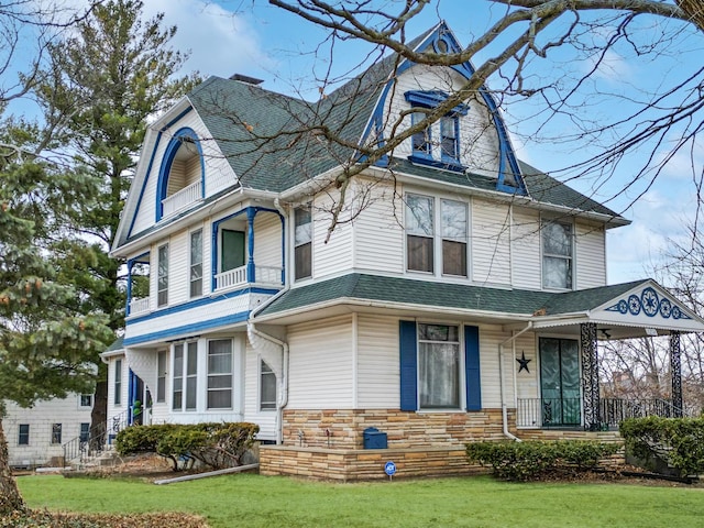 view of front of house featuring stone siding, a front yard, covered porch, and roof with shingles