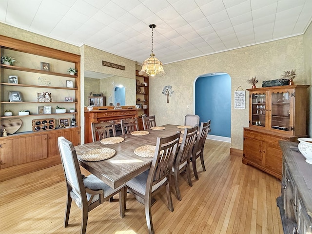 dining room with light wood finished floors, arched walkways, baseboards, built in features, and crown molding