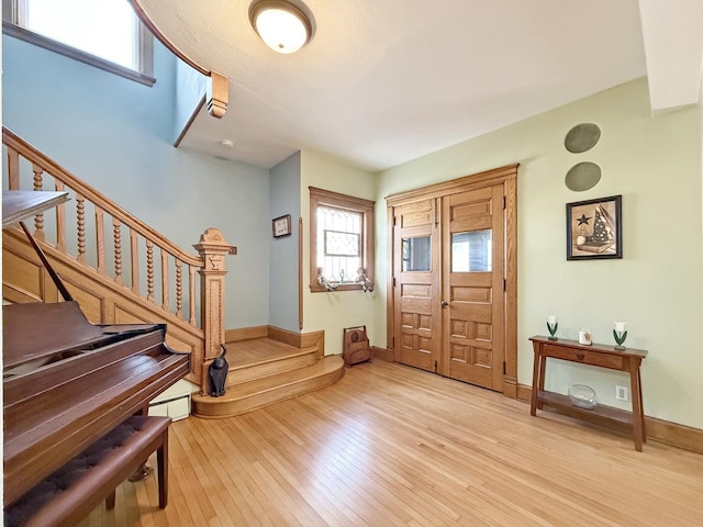 foyer with a baseboard radiator, light wood-style flooring, stairs, and baseboards