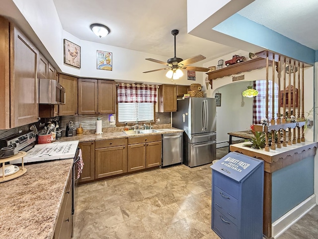 kitchen featuring brown cabinets, stainless steel appliances, decorative backsplash, a ceiling fan, and a sink