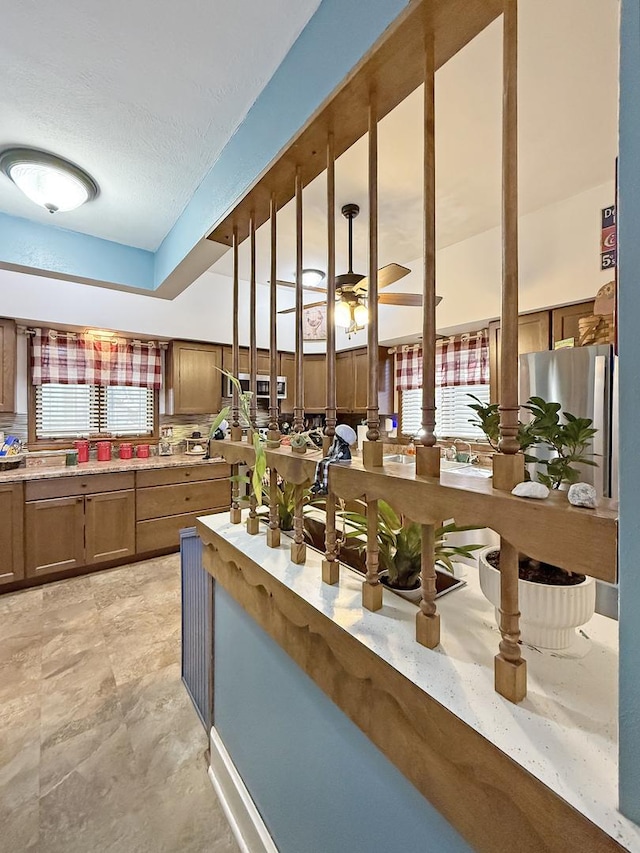 kitchen with light countertops, freestanding refrigerator, brown cabinetry, and a ceiling fan