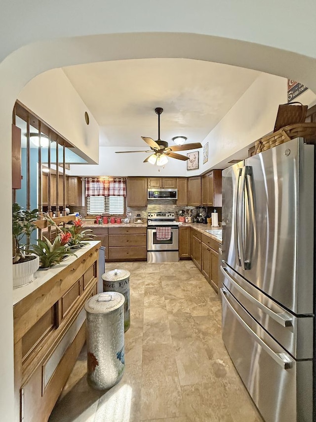 kitchen with arched walkways, ceiling fan, light countertops, appliances with stainless steel finishes, and tasteful backsplash