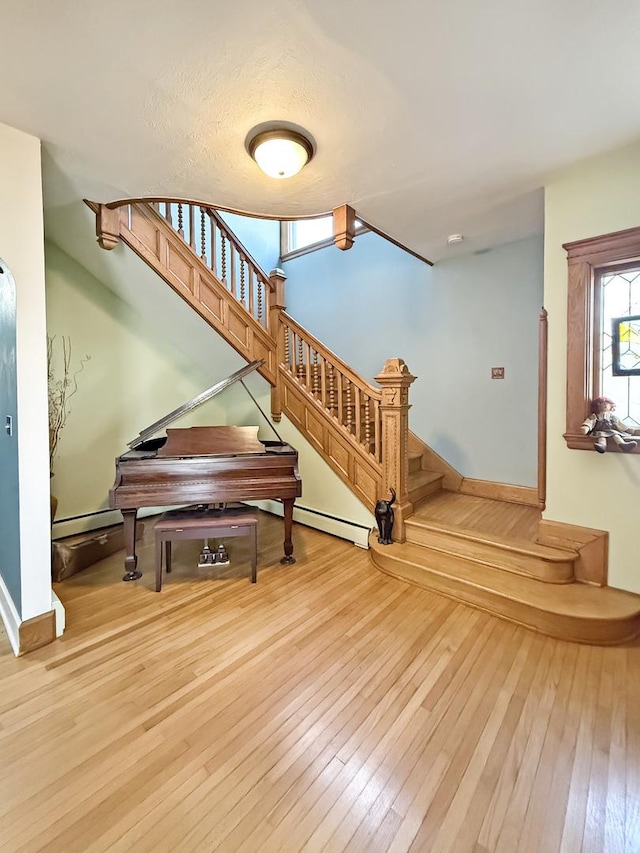 staircase featuring hardwood / wood-style floors, baseboard heating, and baseboards