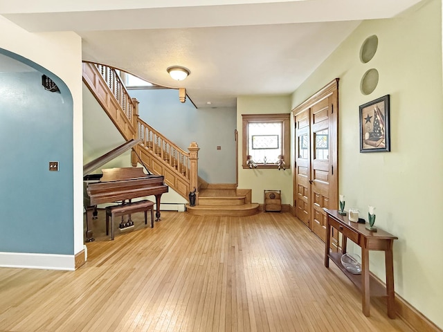 foyer entrance featuring arched walkways, light wood finished floors, baseboard heating, baseboards, and stairs