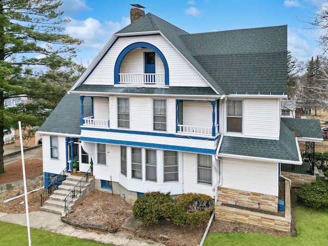 view of front of house with a shingled roof, a chimney, and a balcony