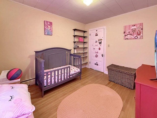 bedroom with crown molding, a baseboard heating unit, and wood finished floors