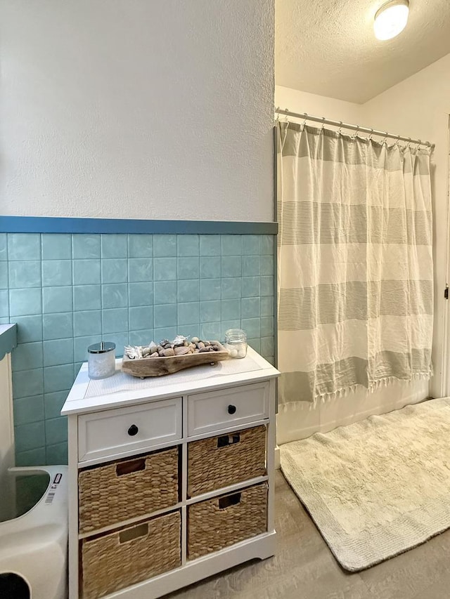 full bath featuring a textured wall, wainscoting, a shower with shower curtain, a textured ceiling, and tile walls