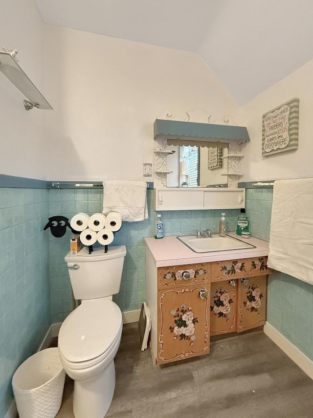 bathroom featuring a wainscoted wall, lofted ceiling, toilet, vanity, and wood finished floors