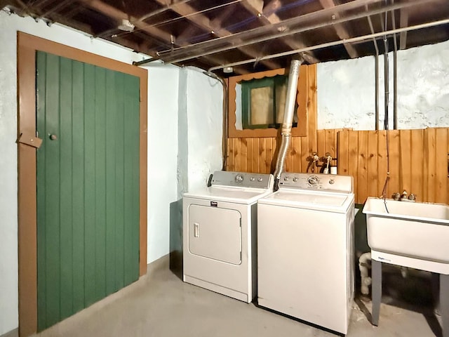 laundry room featuring laundry area, wooden walls, a sink, and independent washer and dryer