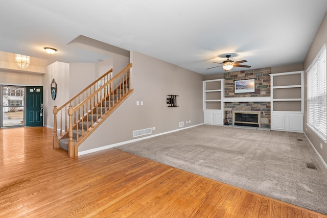 unfurnished living room featuring baseboards, visible vents, wood finished floors, stairs, and a fireplace