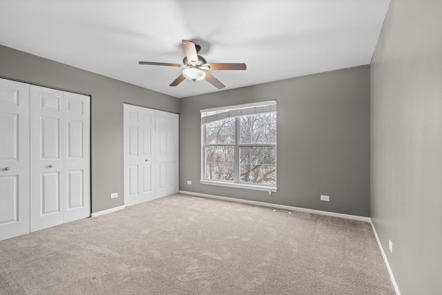 unfurnished bedroom featuring carpet, two closets, visible vents, and baseboards