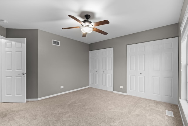 unfurnished bedroom with baseboards, visible vents, carpet flooring, and two closets