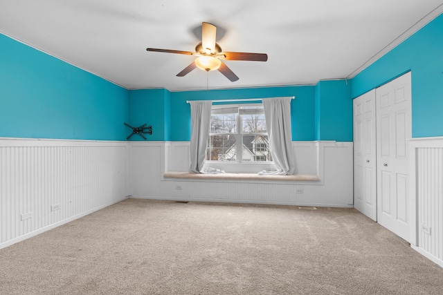 unfurnished bedroom with carpet floors, a wainscoted wall, a ceiling fan, and a closet