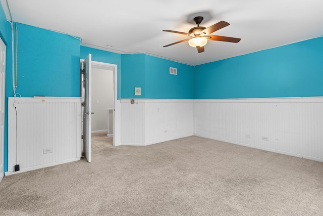 spare room featuring carpet floors, wainscoting, visible vents, and a ceiling fan