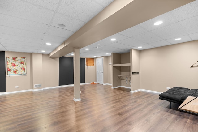 finished basement featuring visible vents, a drop ceiling, baseboards, and wood finished floors