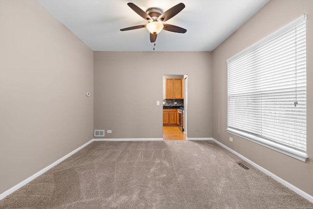 spare room with baseboards, visible vents, ceiling fan, and light colored carpet