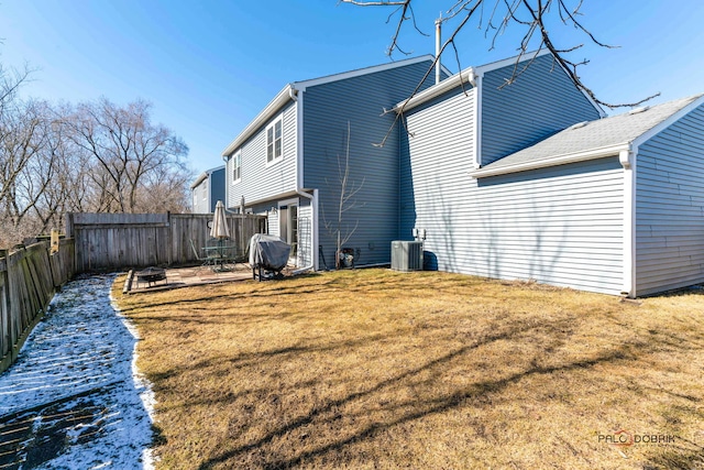 rear view of property featuring cooling unit, a fenced backyard, a yard, and a fire pit