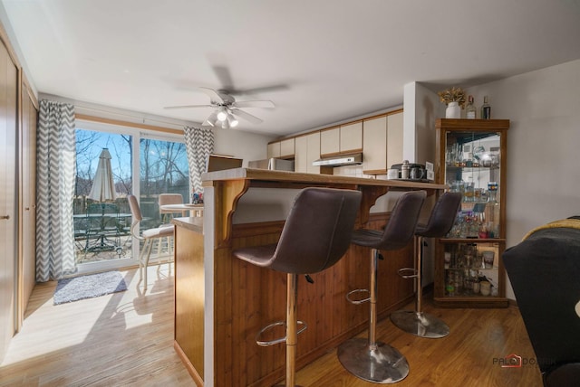 kitchen with light wood-style floors, ceiling fan, a peninsula, under cabinet range hood, and a kitchen bar