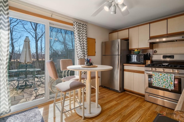 kitchen with light wood-type flooring, under cabinet range hood, stainless steel appliances, and backsplash