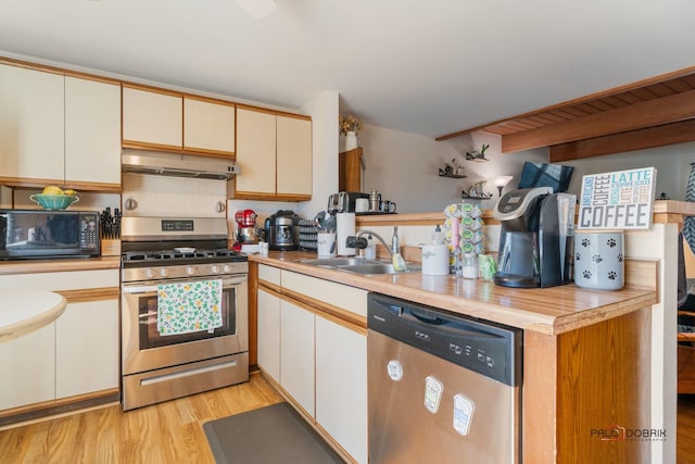 kitchen with under cabinet range hood, a sink, light wood-style floors, light countertops, and appliances with stainless steel finishes