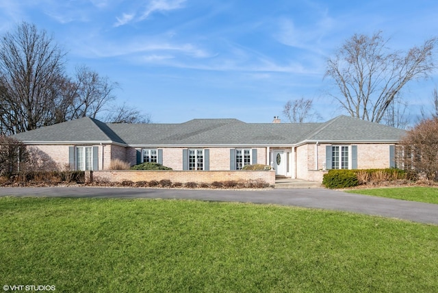 ranch-style house with brick siding, a front lawn, roof with shingles, a chimney, and driveway