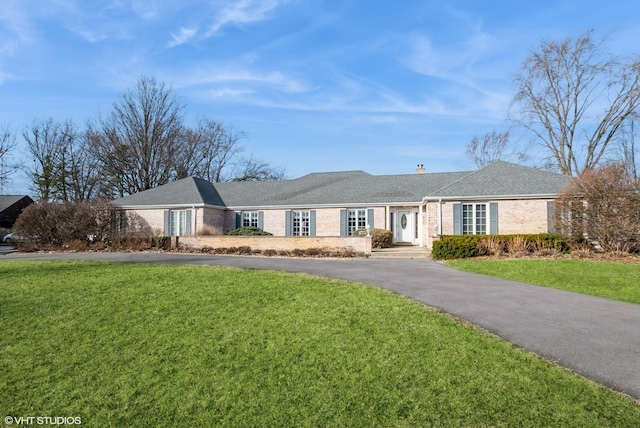 single story home with aphalt driveway, brick siding, a chimney, and a front lawn