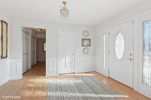 entrance foyer featuring light wood-style floors, wainscoting, and a decorative wall