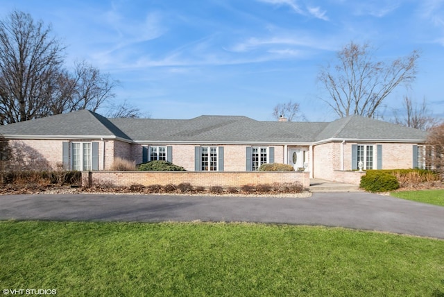 ranch-style home with driveway, a shingled roof, a chimney, a front lawn, and brick siding