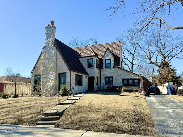 view of front facade with stone siding, a chimney, and fence