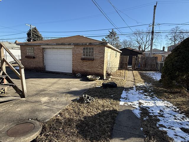 view of property exterior with brick siding, a detached garage, fence, driveway, and an outdoor structure