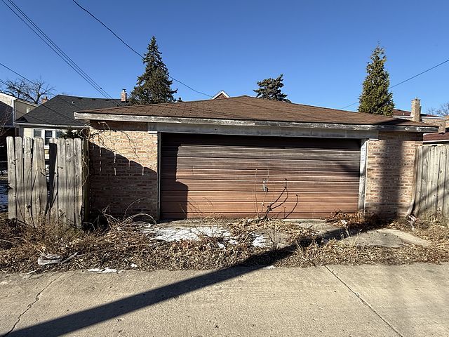 view of property exterior with brick siding, a detached garage, and fence