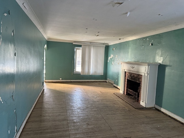 unfurnished living room with a brick fireplace, baseboards, ornamental molding, and arched walkways