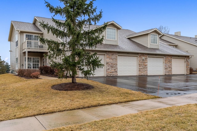 view of front facade with a garage, driveway, stone siding, roof with shingles, and a front yard