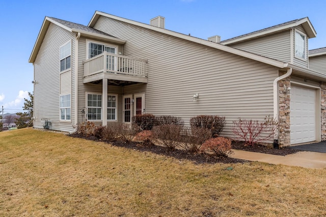 view of side of property featuring a balcony, an attached garage, and a lawn