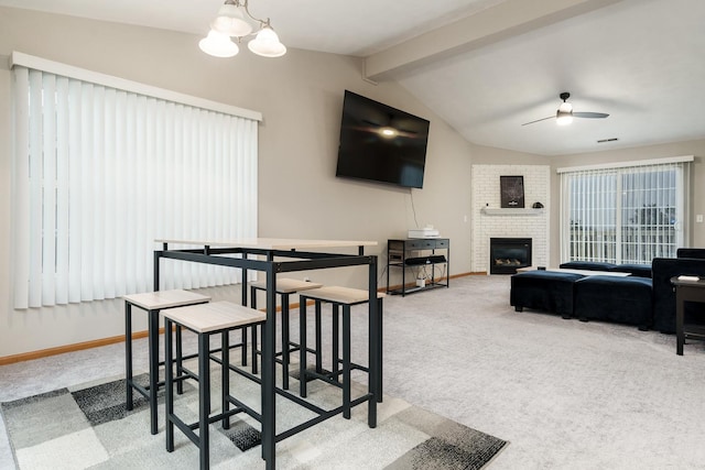 carpeted dining area featuring lofted ceiling with beams, a brick fireplace, baseboards, and ceiling fan with notable chandelier