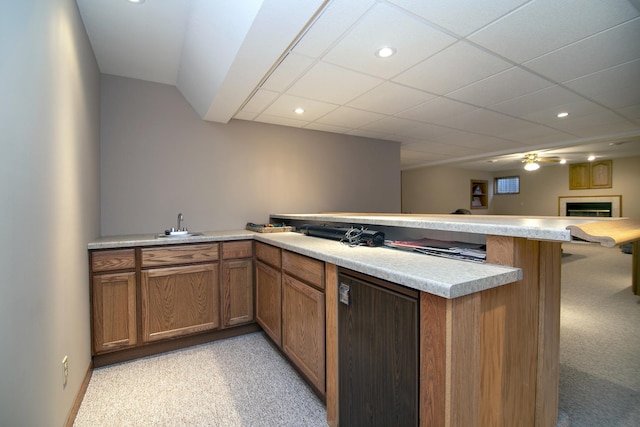 kitchen featuring a peninsula, a sink, light countertops, brown cabinets, and a glass covered fireplace