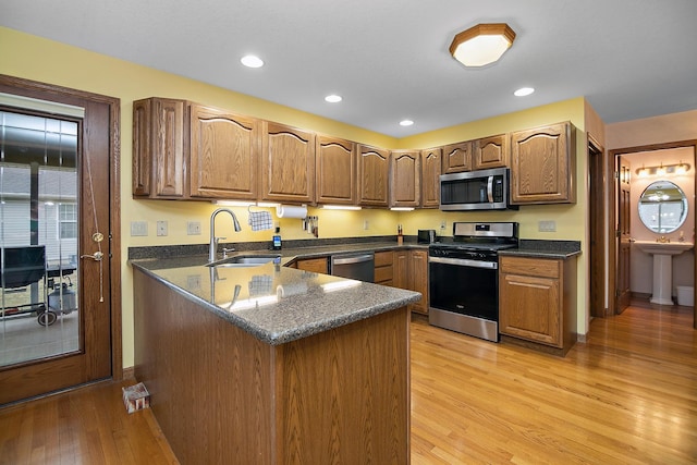 kitchen with a peninsula, stainless steel appliances, light wood-type flooring, a sink, and recessed lighting