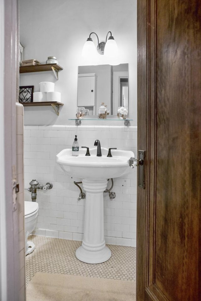 half bath with tile patterned flooring, a wainscoted wall, tile walls, and toilet