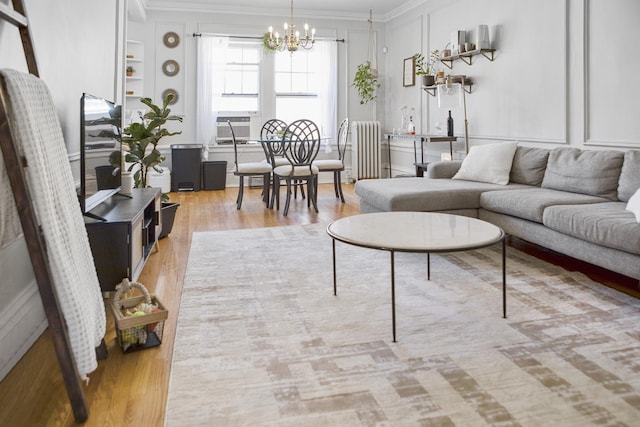 living area featuring radiator, ornamental molding, wood finished floors, an inviting chandelier, and built in shelves