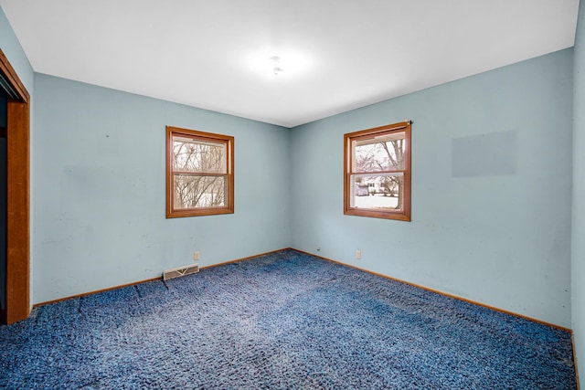 empty room featuring carpet floors, plenty of natural light, visible vents, and baseboards