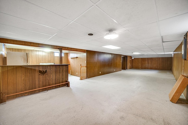 finished below grade area featuring a paneled ceiling, wood walls, and a bar