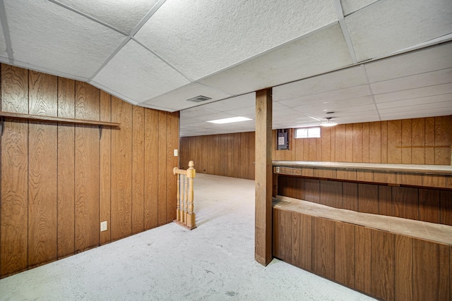 basement featuring carpet floors, a paneled ceiling, visible vents, and wood walls